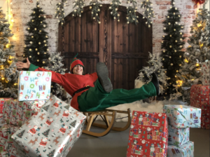 One of Santa's elves sitting on a sleigh surrounded by presents.